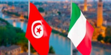 La photo montre l’espace du service des visas de l’Ambassade d’Italie à Tunis. Des demandeurs attendent leur tour devant les guichets. Des agents administratifs traitent les dossiers. Cette scène illustre les démarches habituelles pour obtenir un visa, qui seront temporairement interrompues pendant la période de suspension technique du système informatique.